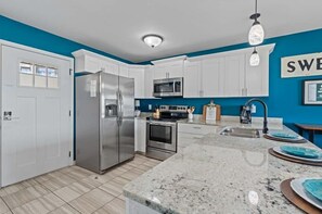 Una cocina moderna con armarios blancos, electrodomésticos de acero inoxidable, encimera de granito y una pared decorada en tono azul.