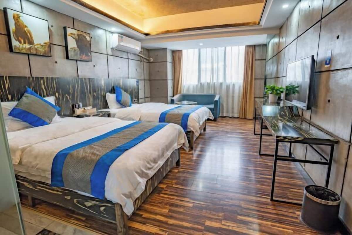 A hotel room with two beds, a desk, a TV, and a large window with curtains.