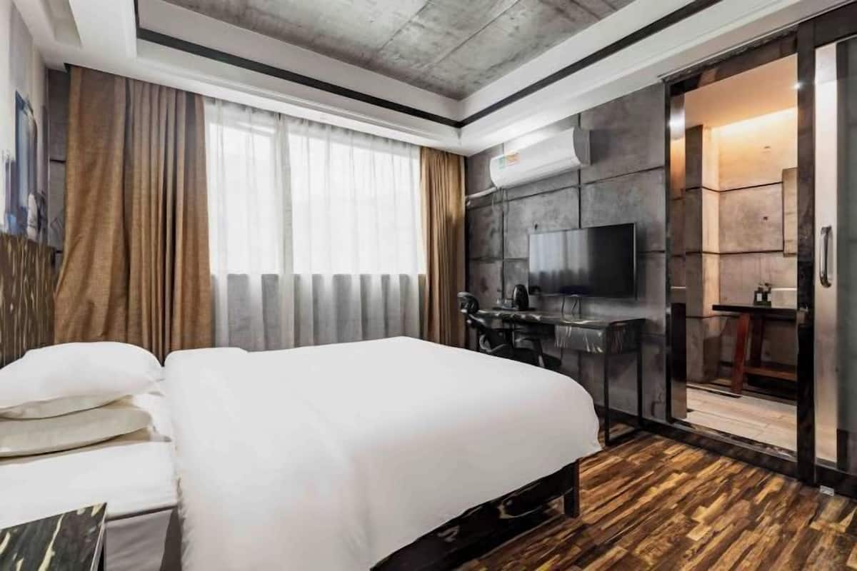 A modern hotel room with a large bed, a desk with a chair, a flat-screen TV mounted on the wall, and a sliding door leading to a bathroom.