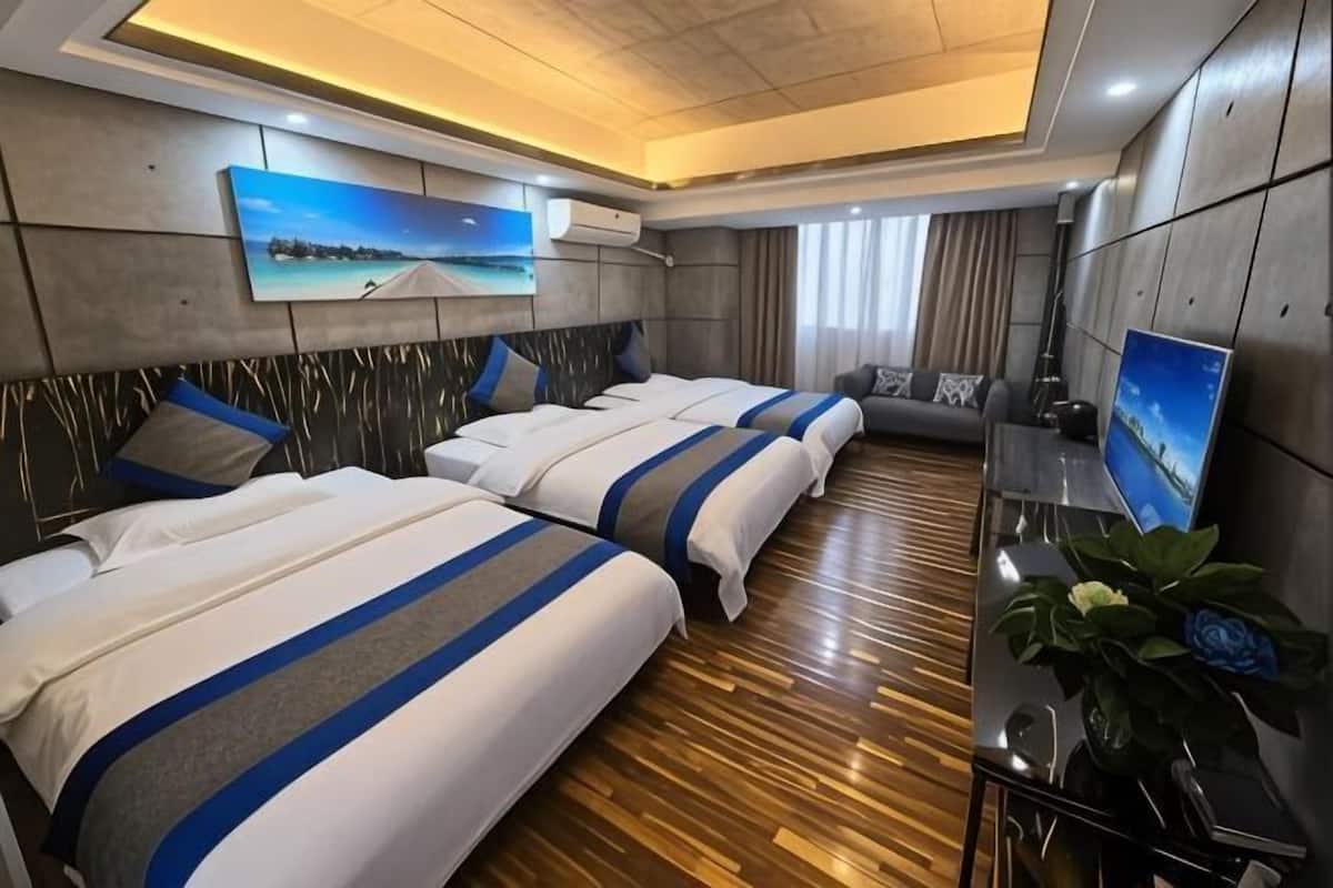 A hotel room with three beds, a TV, a desk, and a large window.