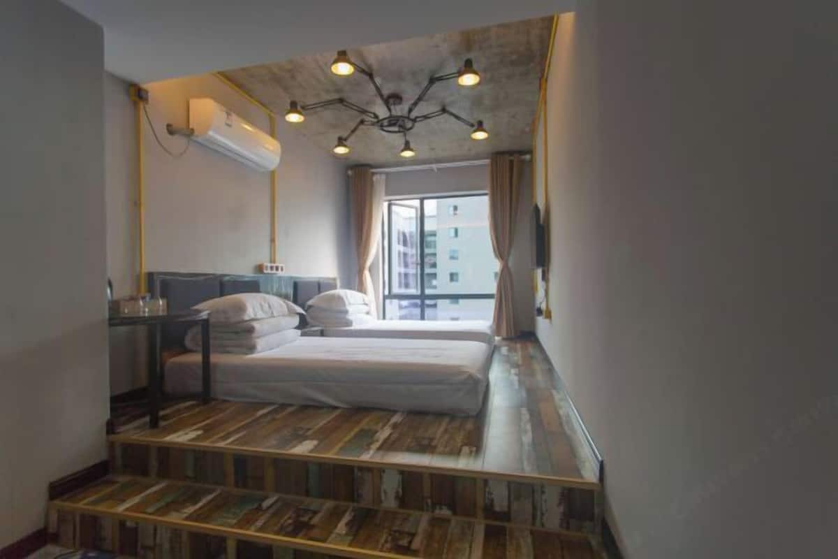 A bedroom with a wooden floor, a bed, a desk, and a window with curtains.