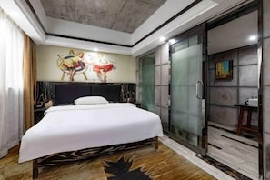 Moderni hotellihuone, jossa on suuri sänky, lasinen suihkuseinä ja taulu seinällä.