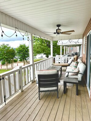 A covered porch with wooden flooring, a ceiling fan, string lights, and outdoor furniture.