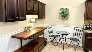 A kitchen with dark wooden cabinets, a wooden table, two chairs, a small round table, and a decorative wreath on the wall. - House# 50 Home Away Home (No pets) (Leesburg)