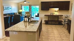 A spacious kitchen with a granite countertop island, dark wooden cabinets, and a view of a dining area with a blue couch and chairs. - House# 50 Home Away Home (No pets) (Leesburg)