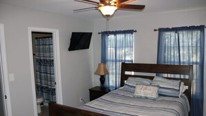 Une chambre à coucher avec un lit en bois, un ventilateur de plafond et une fenêtre ornée de rideaux bleus.