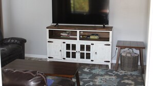 Un salon avec un téléviseur posé sur un meuble en bois, un buffet blanc avec des portes en verre, un canapé en cuir et un tapis à motifs.
