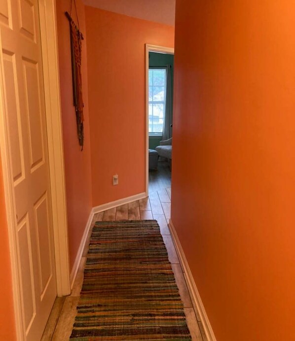 A hallway with orange walls, a striped rug, and a door on the left.
