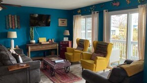 Un salon avec un mur bleu, un canapé, un fauteuil jaune, une petite table et un téléviseur.