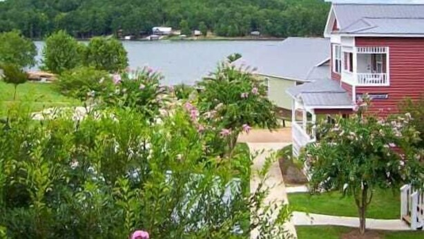 Une maison rouge avec un porche, entourée d’une végétation luxuriante et bordée d’un lac.