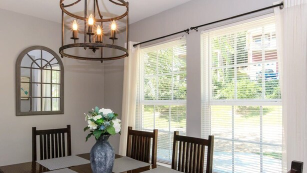 A dining room with a wooden table, four chairs, a vase with flowers, and a chandelier.