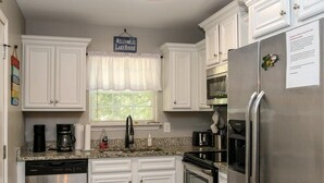 A modern kitchen with white cabinets, stainless steel appliances, and a window with a white valance.