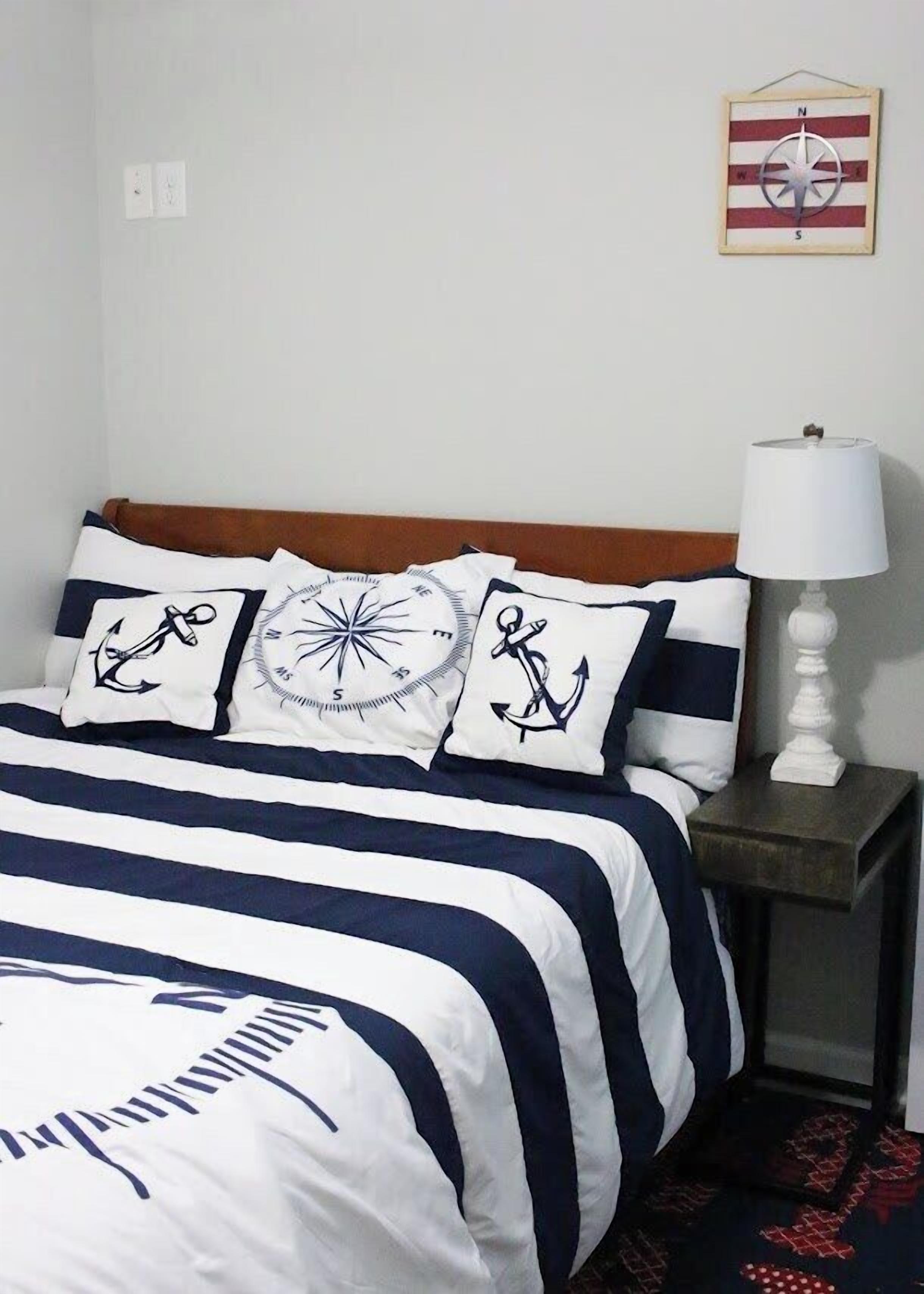 A neatly made bed with striped bedding, a compass wall decoration, and a lamp on a bedside table.