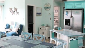 Un comedor con una mesa y sillas, una cocina equipada con un refrigerador y una sala de estar con un sofá y sillas.