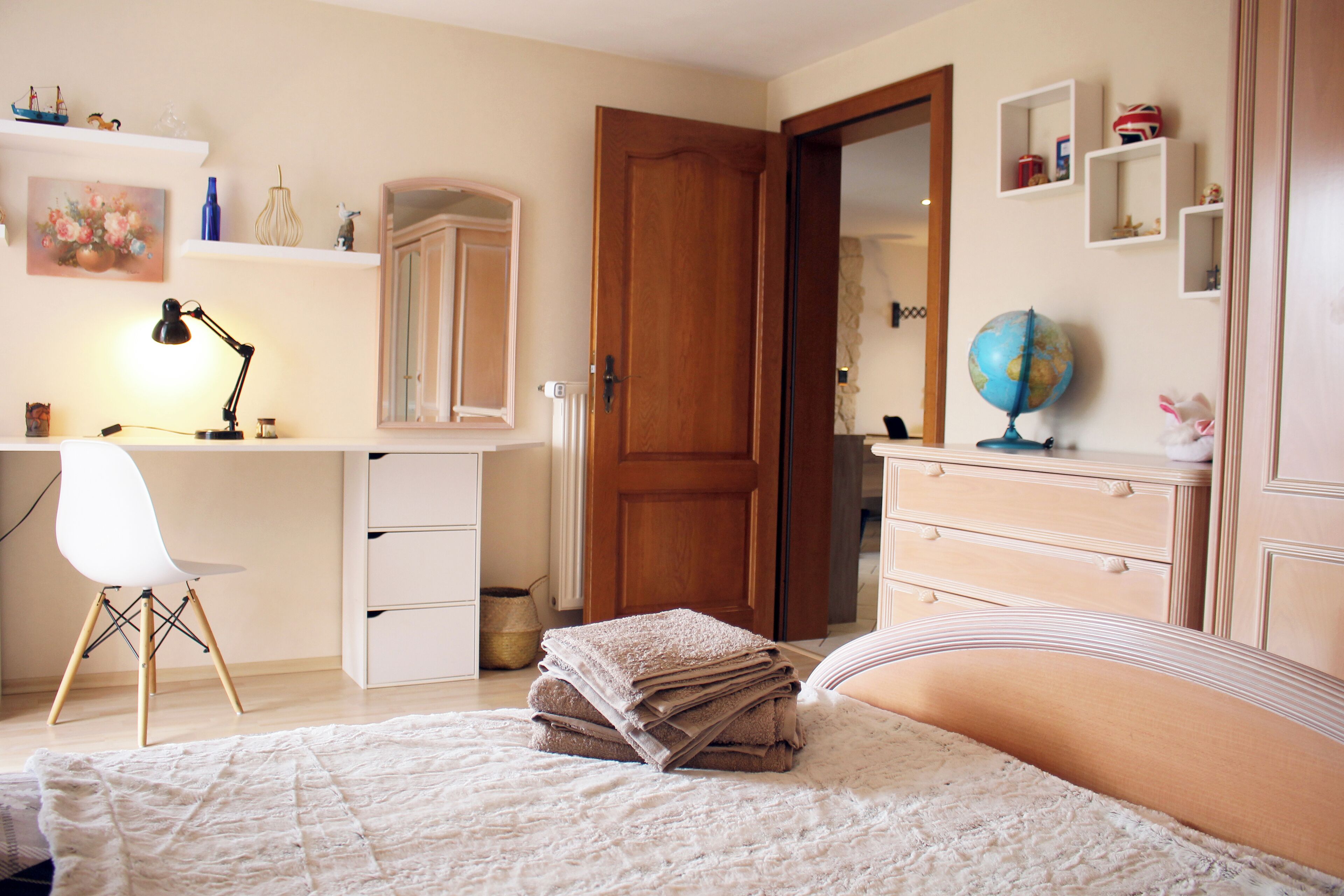 Un dormitorio con cama, escritorio, silla, armario, espejo y un globo terráqueo.