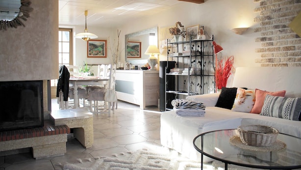 A living room with a fireplace, a sofa, a glass coffee table, and a dining area with chairs and a table.