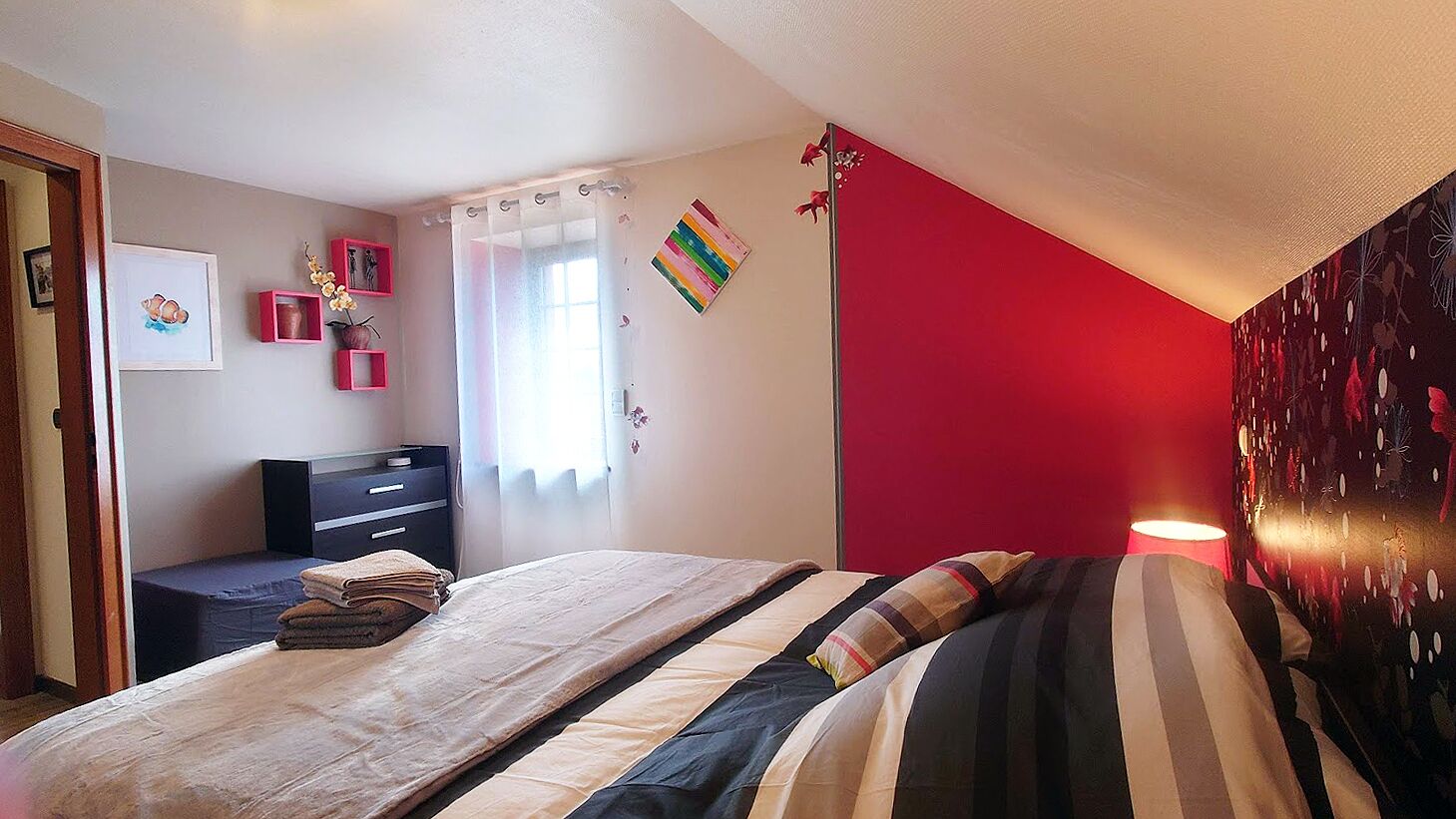 A bedroom with a bed, a dresser, a desk, and a red accent wall.