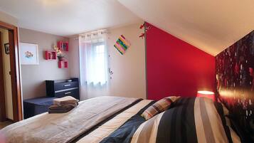 A bedroom with a bed, a dresser, a desk, and a red accent wall.