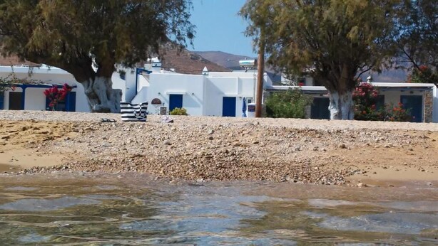 A coastal area with white buildings, some with blue doors, and a rocky shoreline. - Studios Agira Serifos (Serifos)