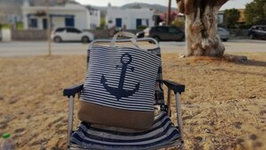 A beach chair with a striped fabric and an anchor design, positioned on sandy ground with a tree and parked cars in the background. - Studios Agira Serifos (Serifos)