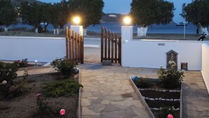 A stone pathway leading to a gated entrance with a small shrine, surrounded by flower beds and trees. - Studios Agira Serifos (Serifos)