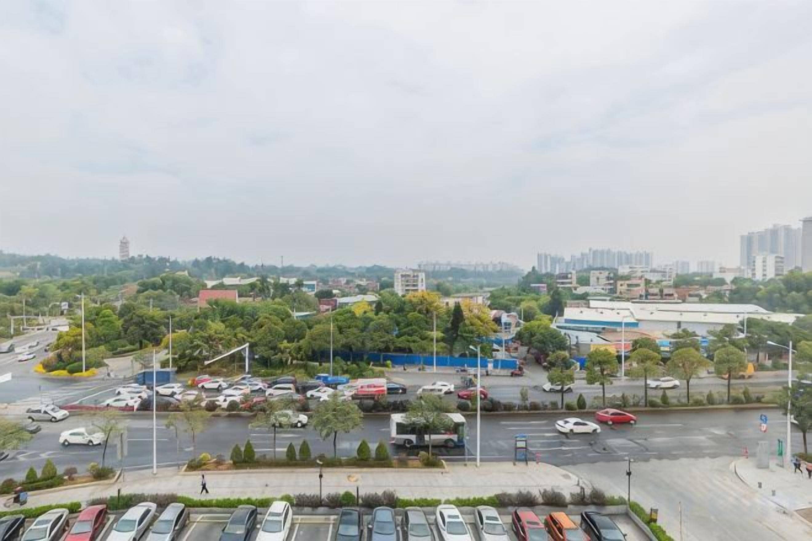 Un parcheggio con diverse auto, una strada trafficata e edifici sullo sfondo.