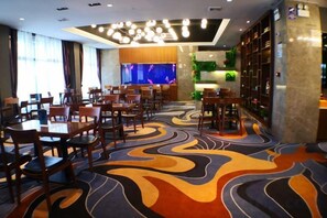 Un vestíbulo de hotel con varias mesas y sillas para comer, una alfombra estampada, una zona de bar y un gran acuario.