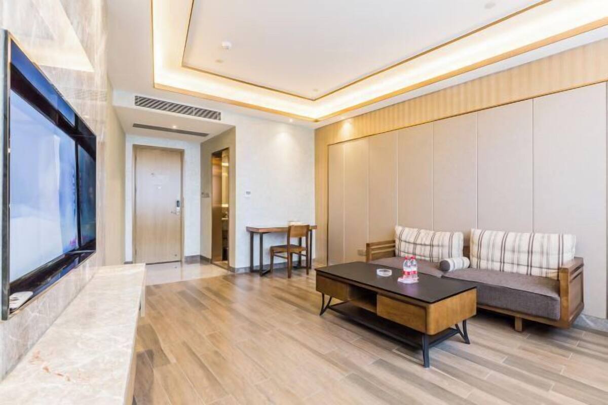 Una habitación de hotel moderna con una gran televisión de pantalla plana, una mesa de centro de madera, un sofá y una pequeña mesa con sillas.