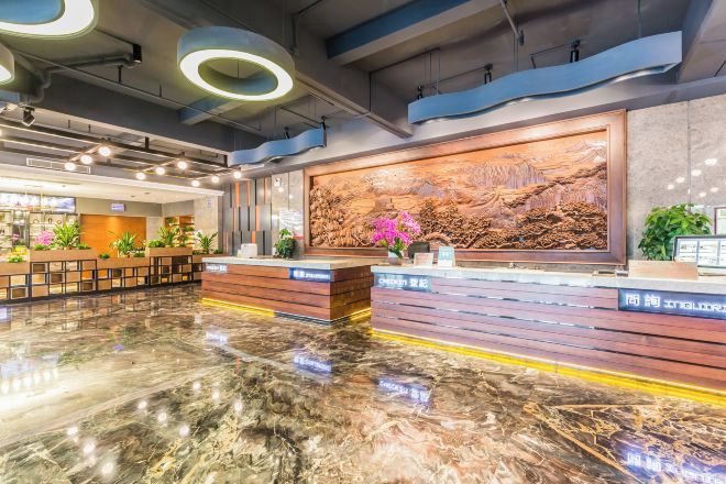 Un moderno vestíbulo de hotel con piso de mármol, mostrador de recepción de madera y un amplio mural en la pared.