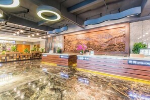 A modern hotel lobby with a marble floor, wooden reception desk, and a large wall mural. - Rimei Hotel (Foshan Sanshui New Power) (Foshan)