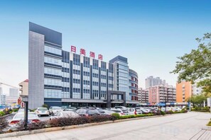 A hotel with a modern facade, multiple floors, and a parking lot.