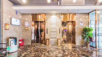 A hotel lobby with a marble floor, a reception desk, a television, and a plant.
