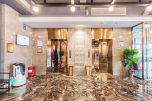 Un hall d’hôtel avec un sol en marbre, un comptoir d’accueil, un téléviseur et une plante.