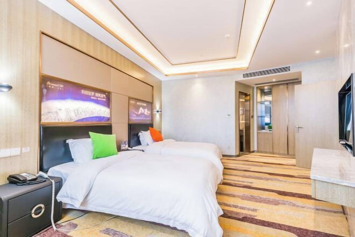 Habitación de hotel con dos camas, televisión, escritorio y baño visible a través de una puerta abierta.