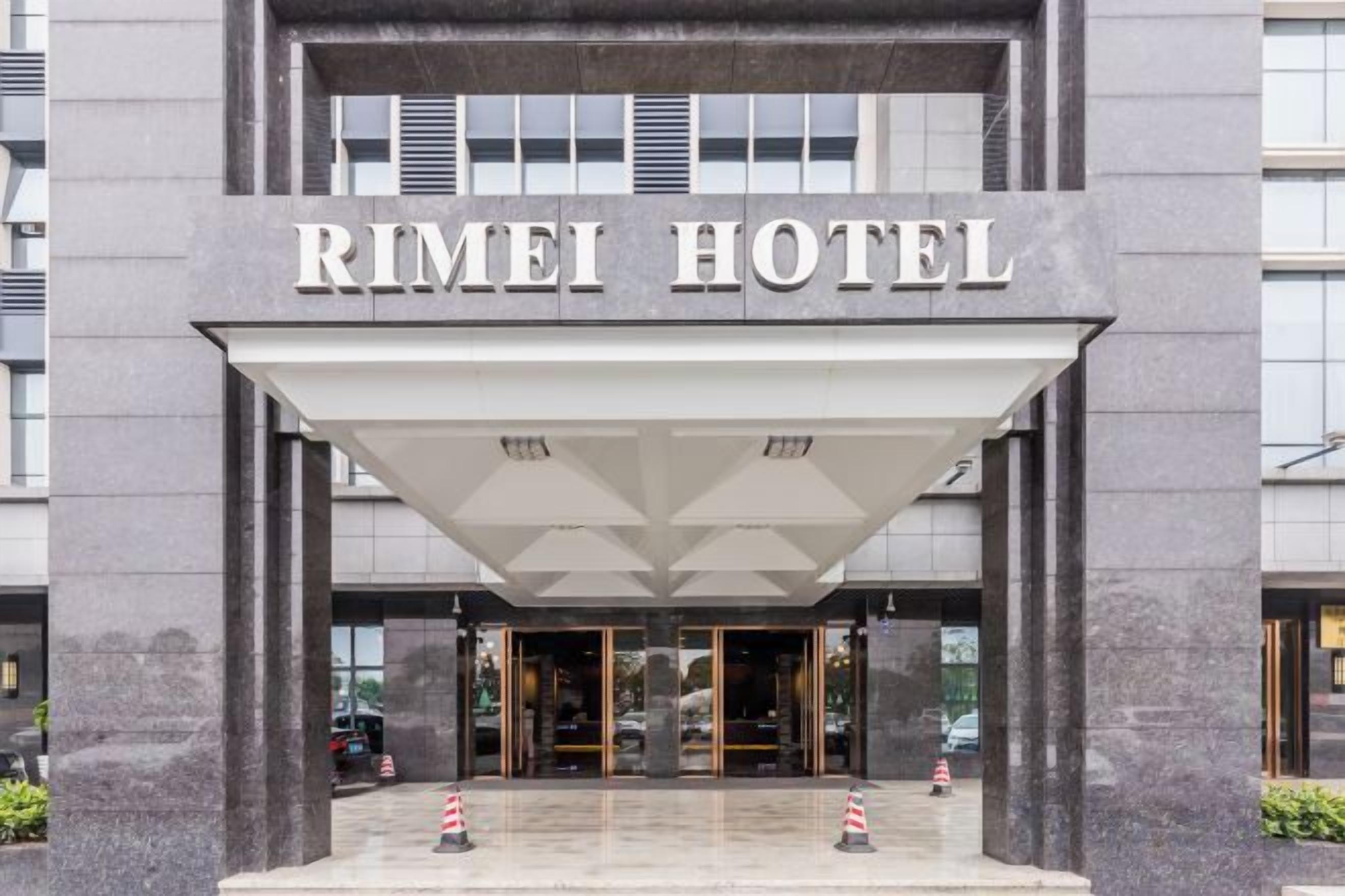 Der Eingang des RIMEI HOTEL mit einer modernen Fassade, großen Glasüren und einem überdachten Bereich.