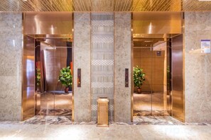 Un ascensor moderno con puertas de cristal, suelo de mármol y un panel decorativo vertical.