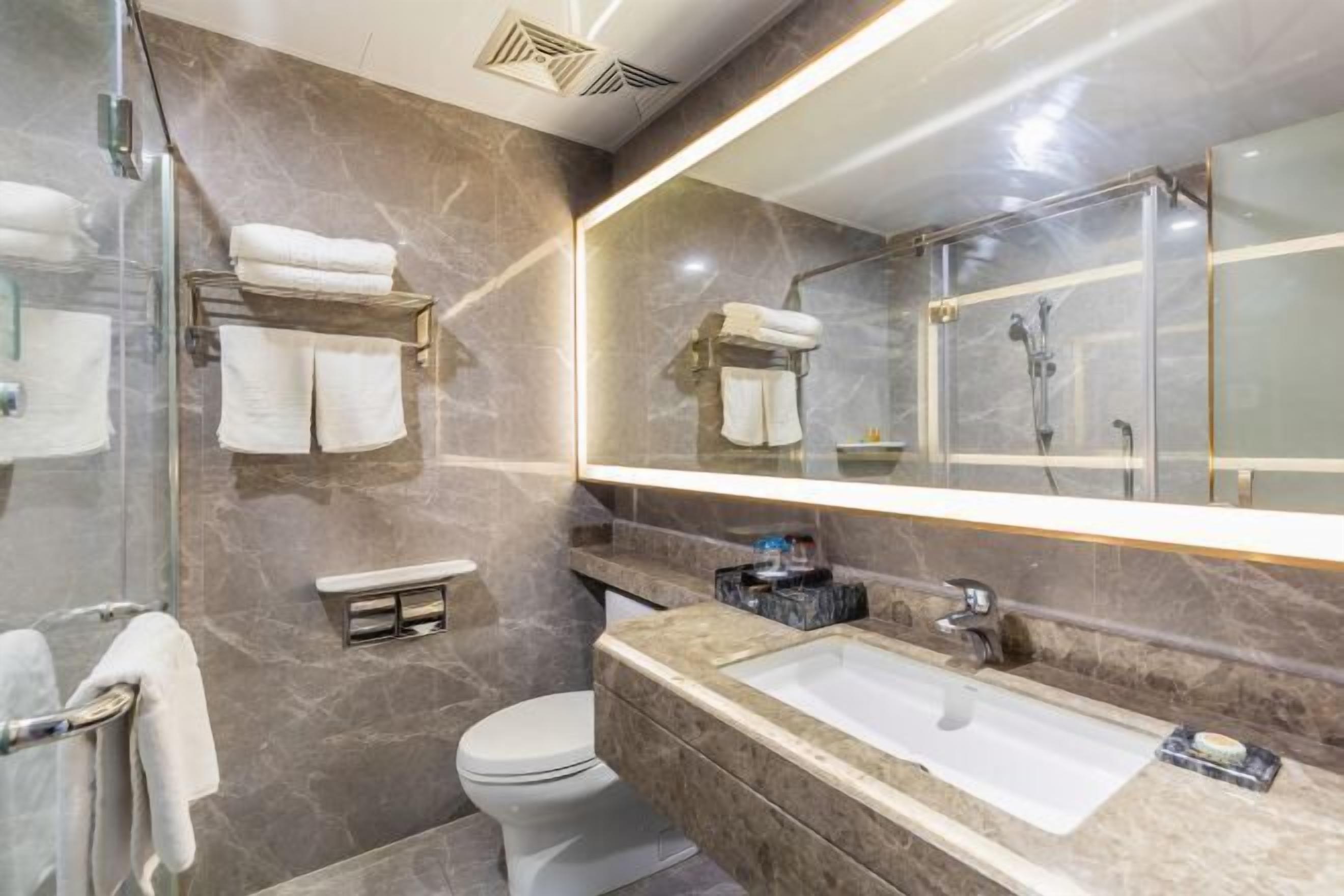 A bathroom with a marble wall, a glass shower enclosure, a white toilet, and a large sink with a mirror above it.