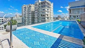 Ein Dachpool mit einem gemusterten Fliesenbelag, umgeben von modernen Gebäuden und blauem Himmel.