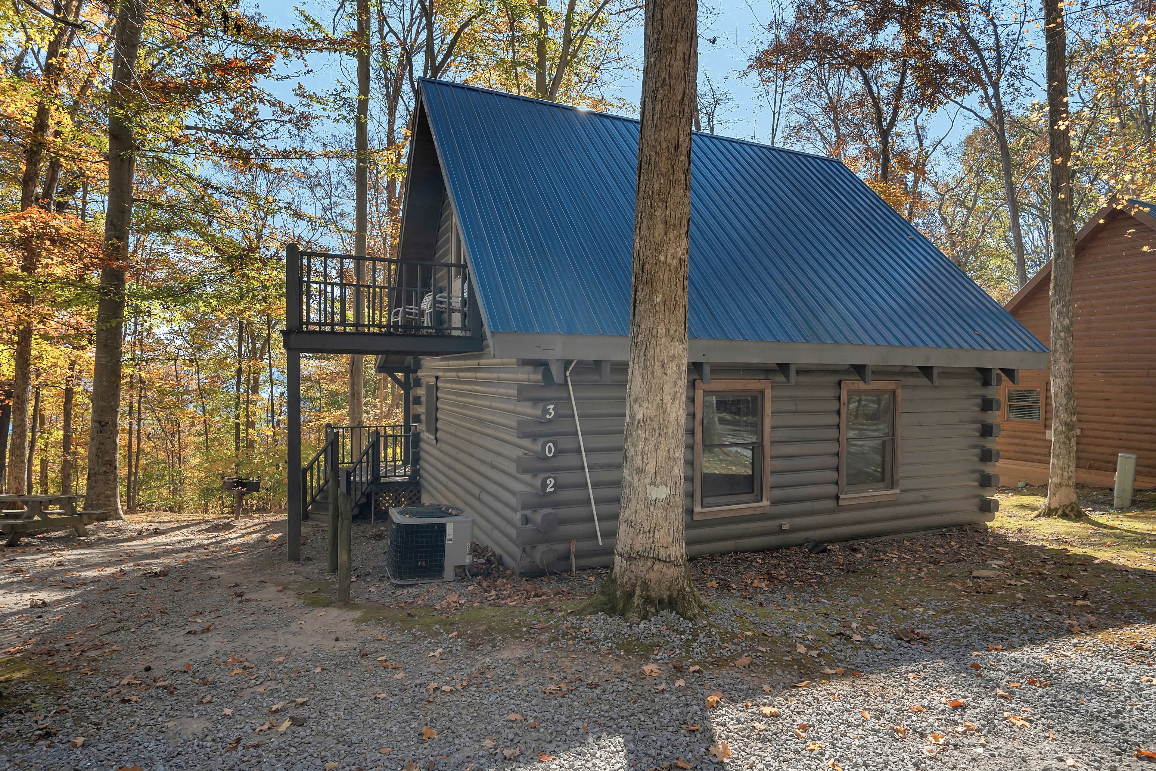 A log cabin with a balcony, a gravel path, and a forested background.