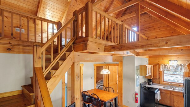 Interior de una cabaña de madera con comedor, cocina y una escalera.