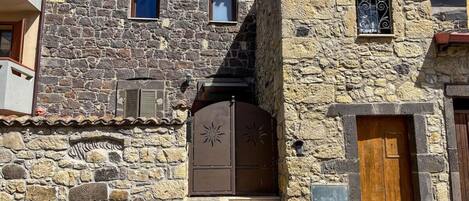 Un edificio de piedra con una entrada central, una ventana pequeña y una puerta con una celosía metálica decorativa.