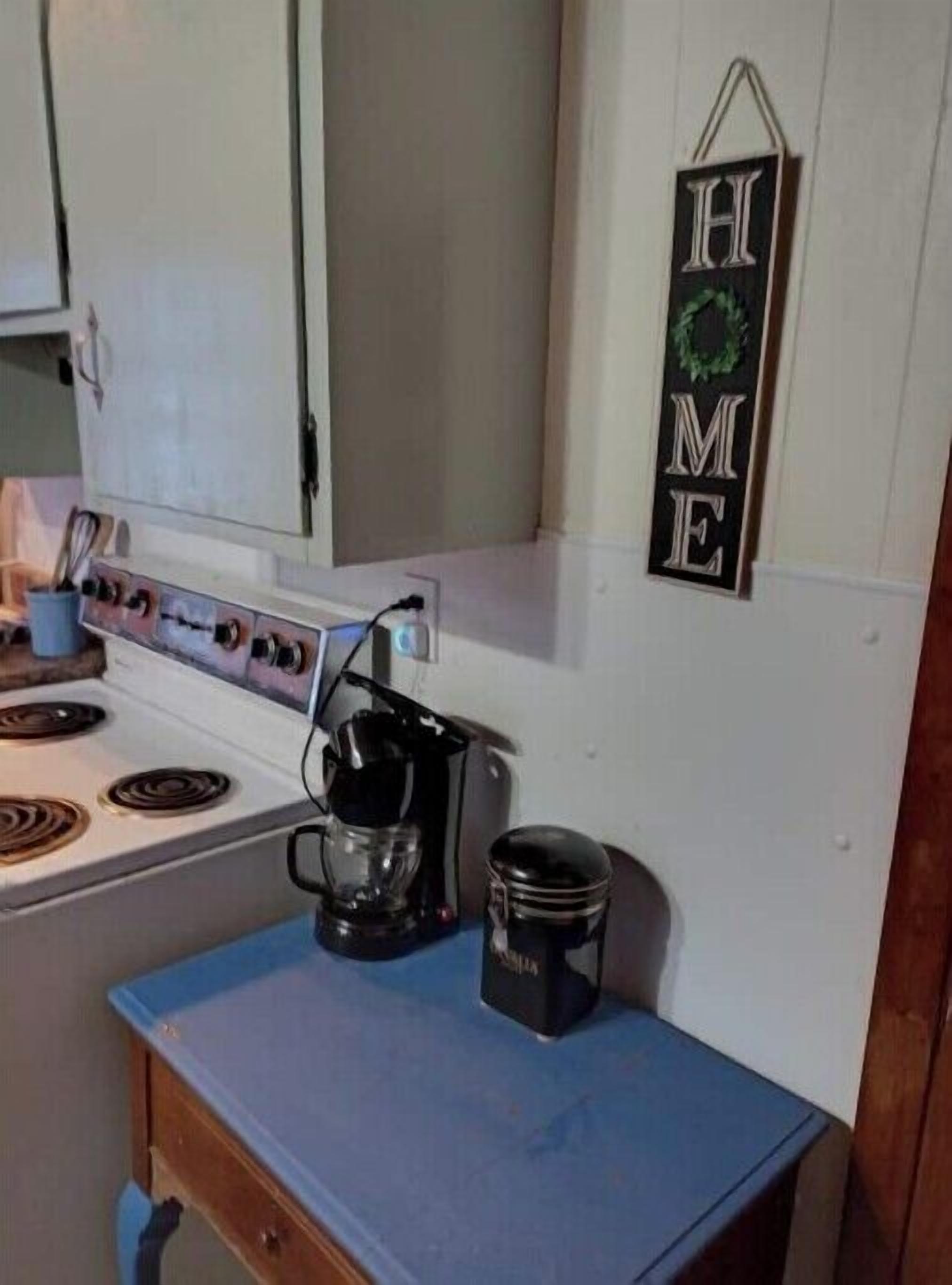 A kitchen with a stove, coffee maker, and a 'HOME' sign on the wall.