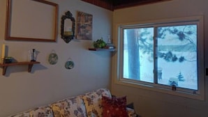 Ein Zimmer mit Holzbalkendecke, einem Fenster mit Blick auf Schnee, einem Blumensofa und Wanddekorationen, darunter ein Spiegel und gerahmte Bilder.