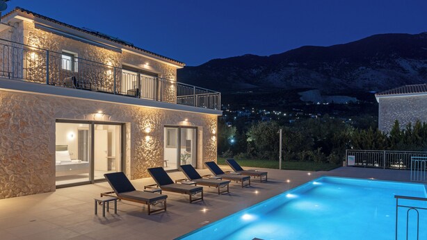 Eine moderne Villa mit Schwimmbad, Natursteinfassade und Blick auf die Berge.