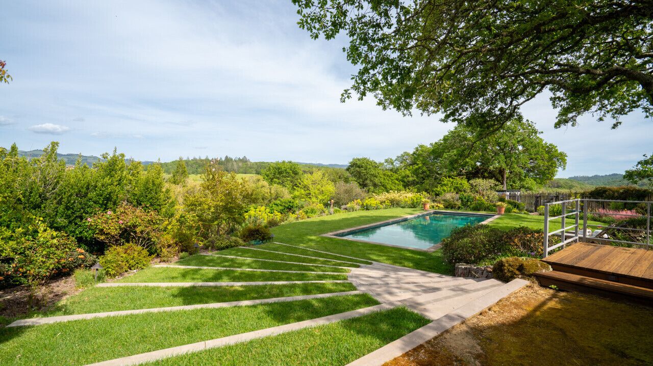 A landscaped garden with a swimming pool, a wooden deck, and a stone pathway leading to the pool.