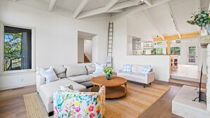 A spacious living room with a large sectional sofa, a round coffee table, and a colorful armchair. A kitchen area is visible in the background.