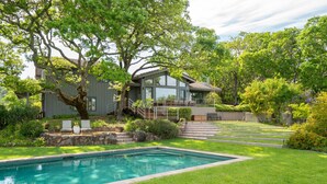 A modern house with a swimming pool, surrounded by lush greenery and trees.