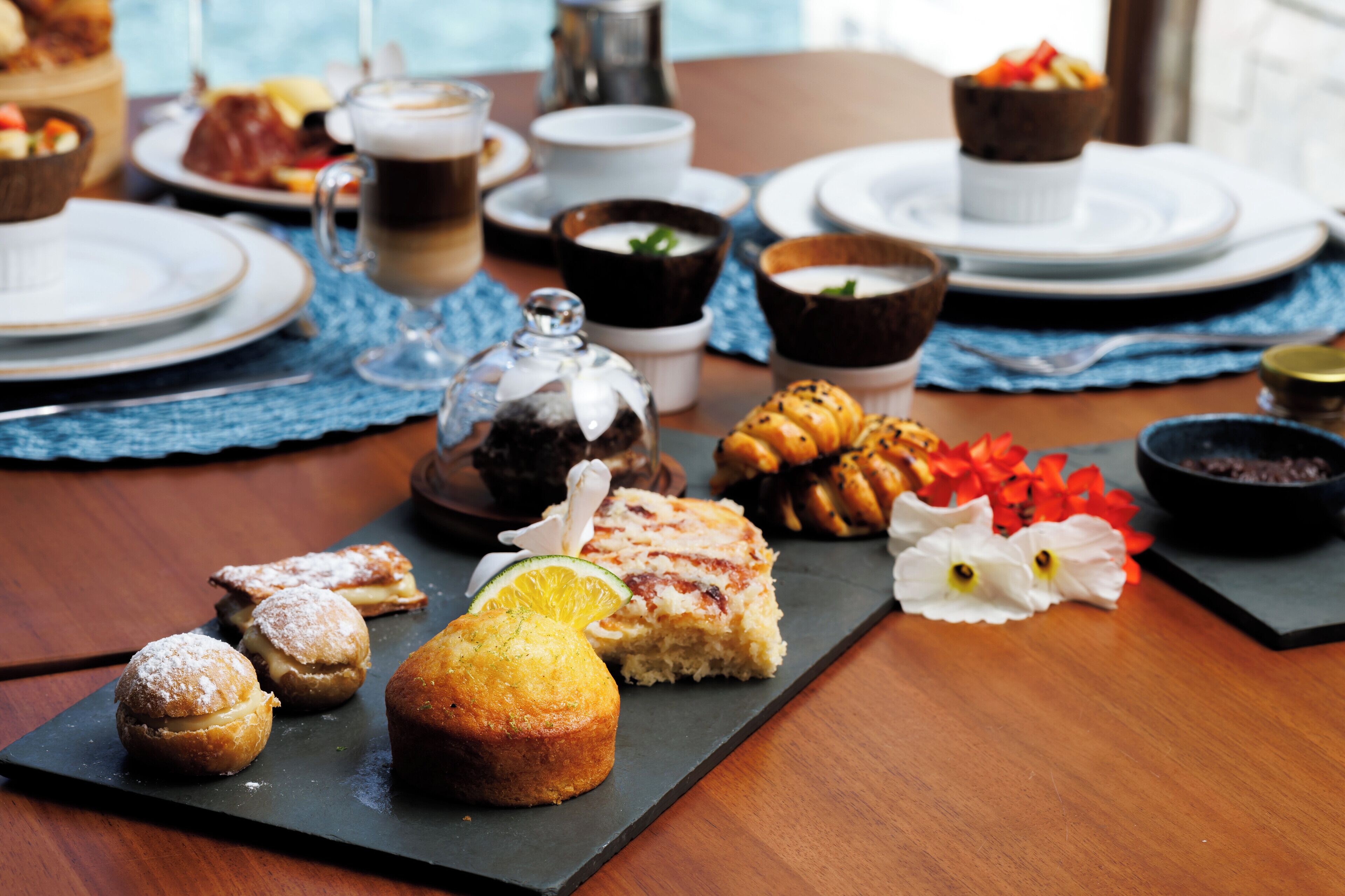 A table set with various pastries, desserts, and beverages, suggesting a breakfast or brunch setting.