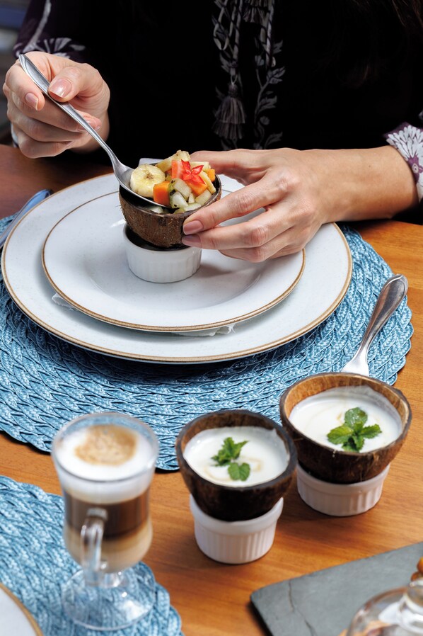 A person eating a meal with a spoon, a plate, and a cup with a spoon. There are also two small cups with a spoon and a glass of a beverage. - Almareia Boutique Hotel (Tamandaré)