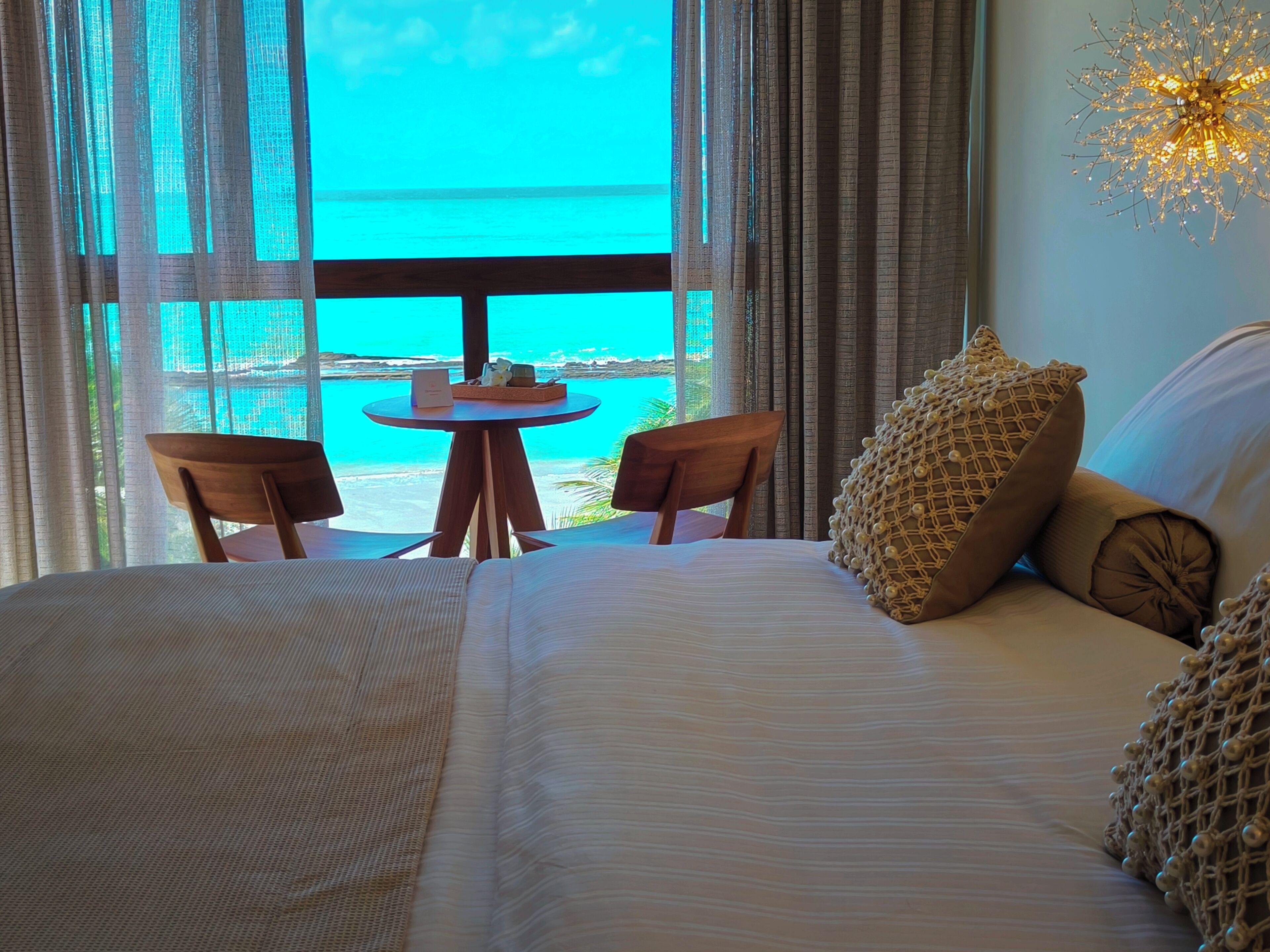 Habitación de hotel con una cama, dos sillas, una mesita y vista al océano.